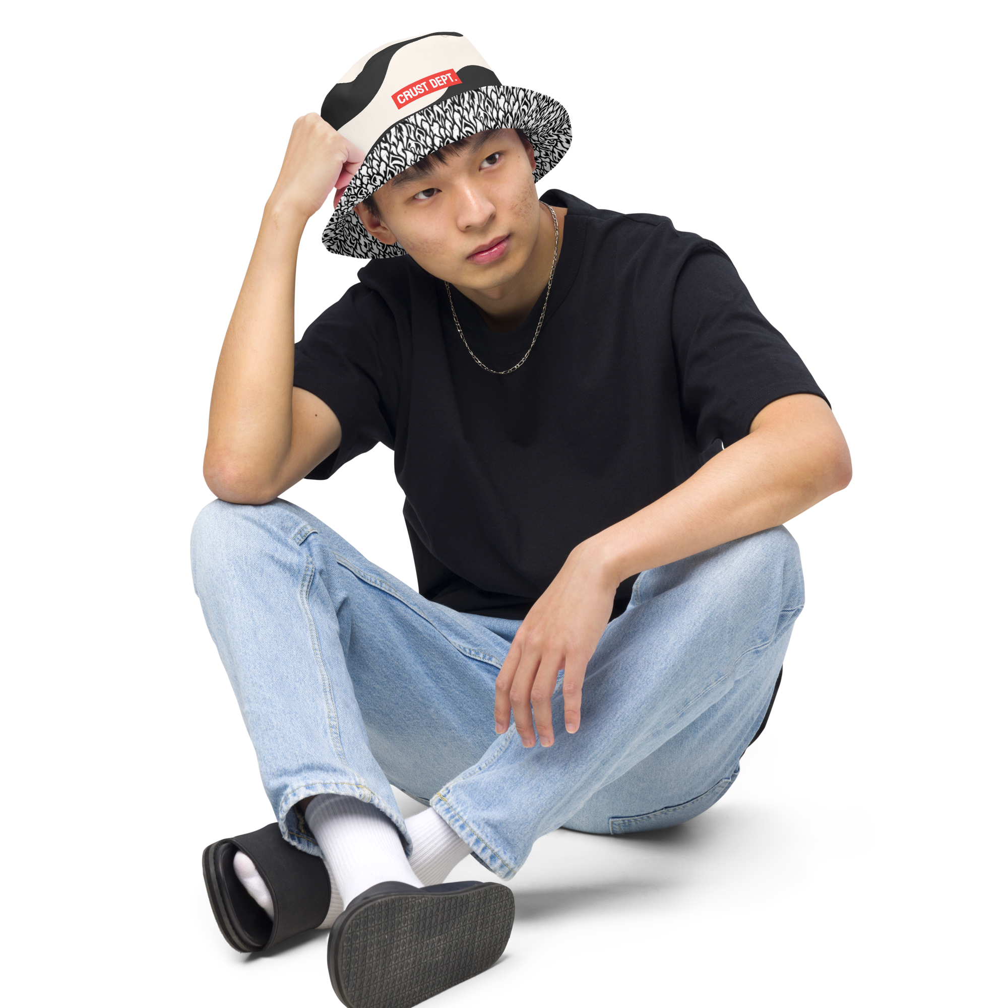 Person wearing a black t-shirt, light blue jeans, and a patterned cap on a white background