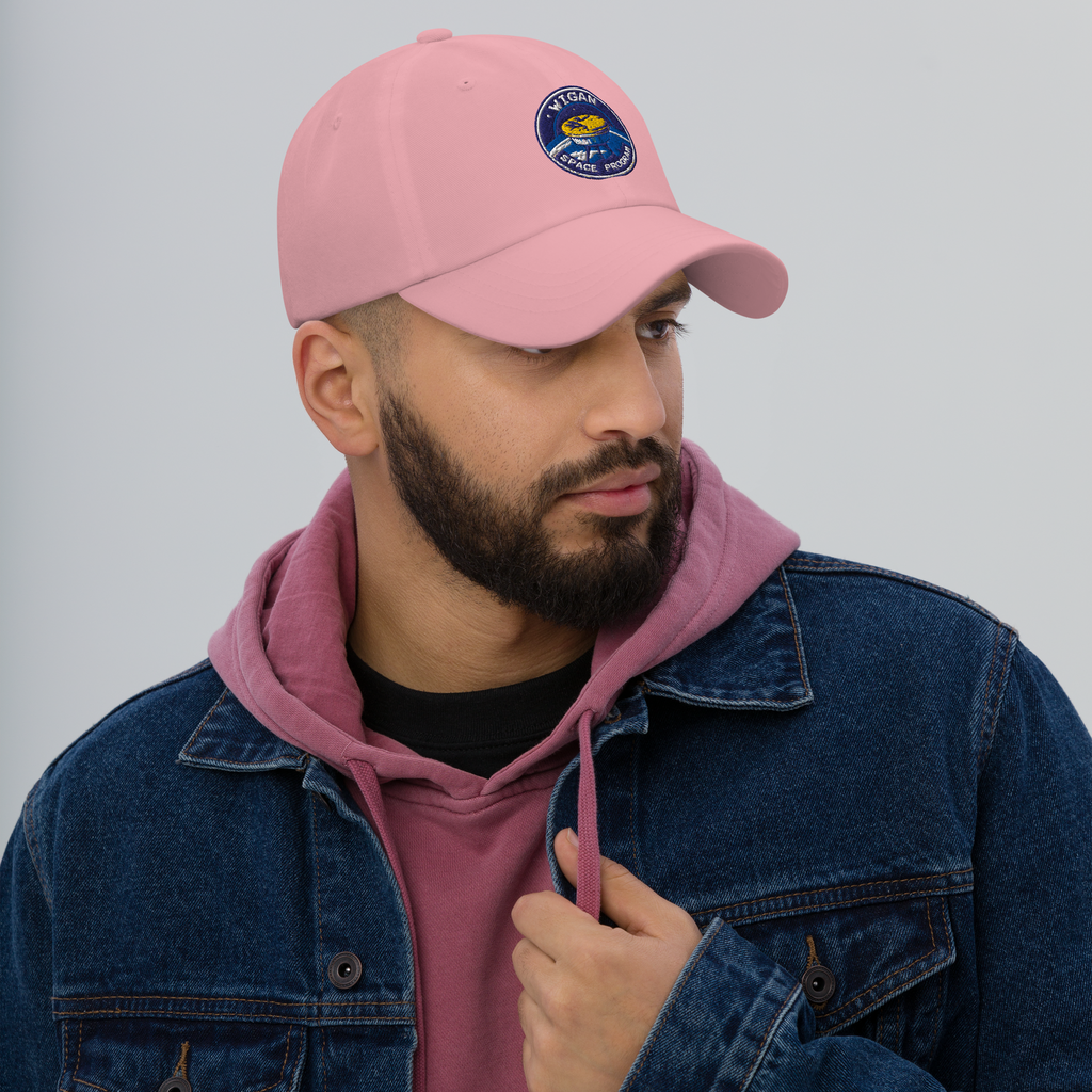 Man wearing a pink cap with a logo, purple hoodie, and blue denim jacket on a gray background