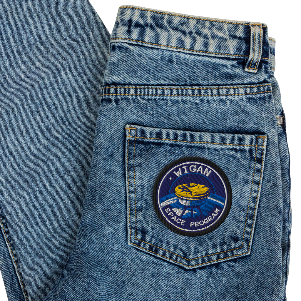 Blue denim jeans with a patch on the back pocket featuring 'Wigan Space Program' design.