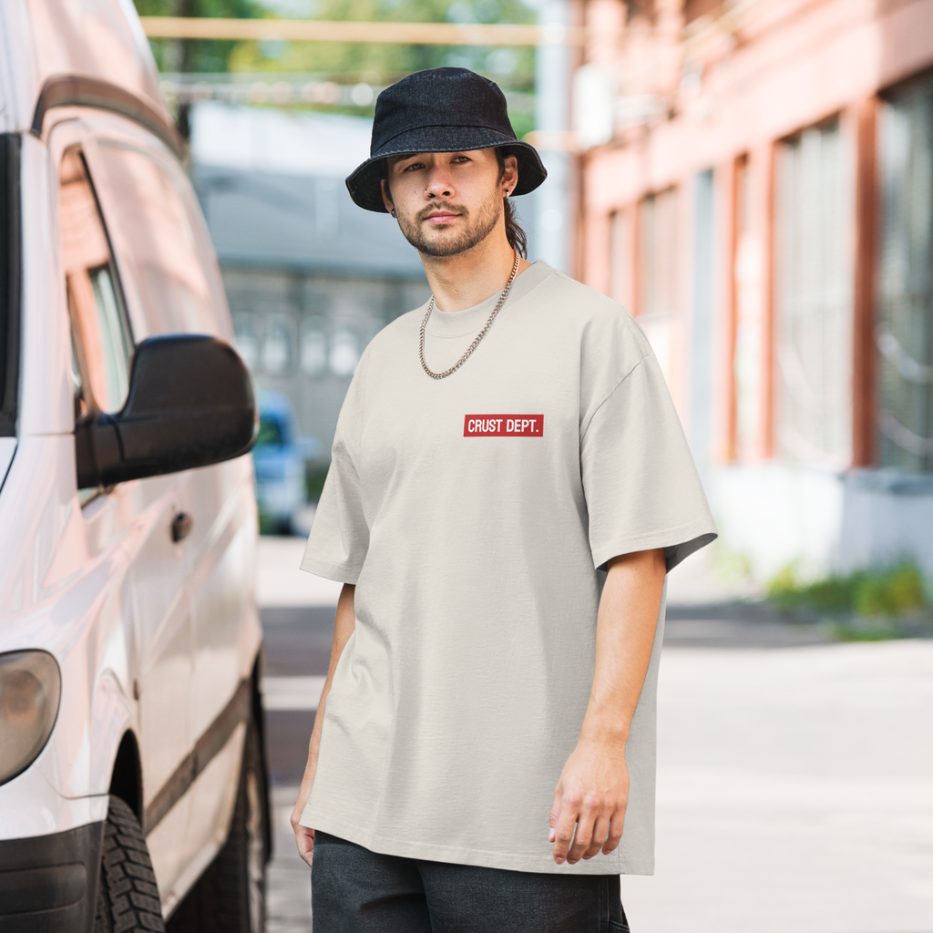 Man wearing a bone white t-shirt with a red Crust Dept. logo and black bucket hat standing next to a van.