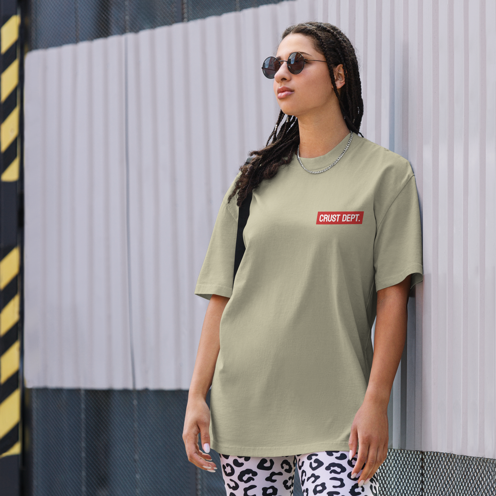Person wearing a eucalyptus green t-shirt with a Crust Dept. logo and patterned pants against a striped wall.